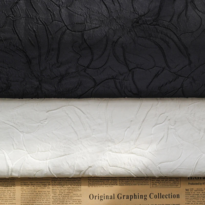 Two rolls of Longon Craft Floral Embossed Jacquard Brocade Fabric—one black, one white—lie side by side on newspaper, showcasing a raised 3D solid flower pattern in polyester for party costumes and tailored suits.