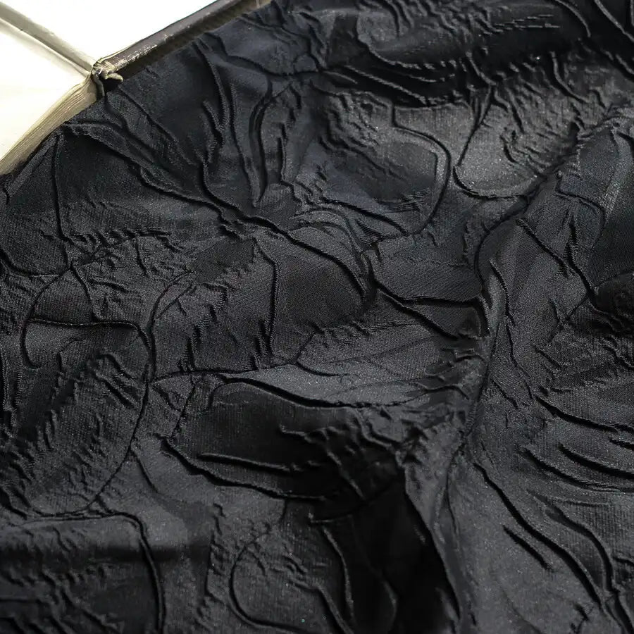 Close-up of Longon Craft's Floral Embossed Jacquard Brocade Fabric, featuring a 3D solid color flower pattern on black polyester with raised textures and subtle sheen—ideal for party costumes and tailored suits.
