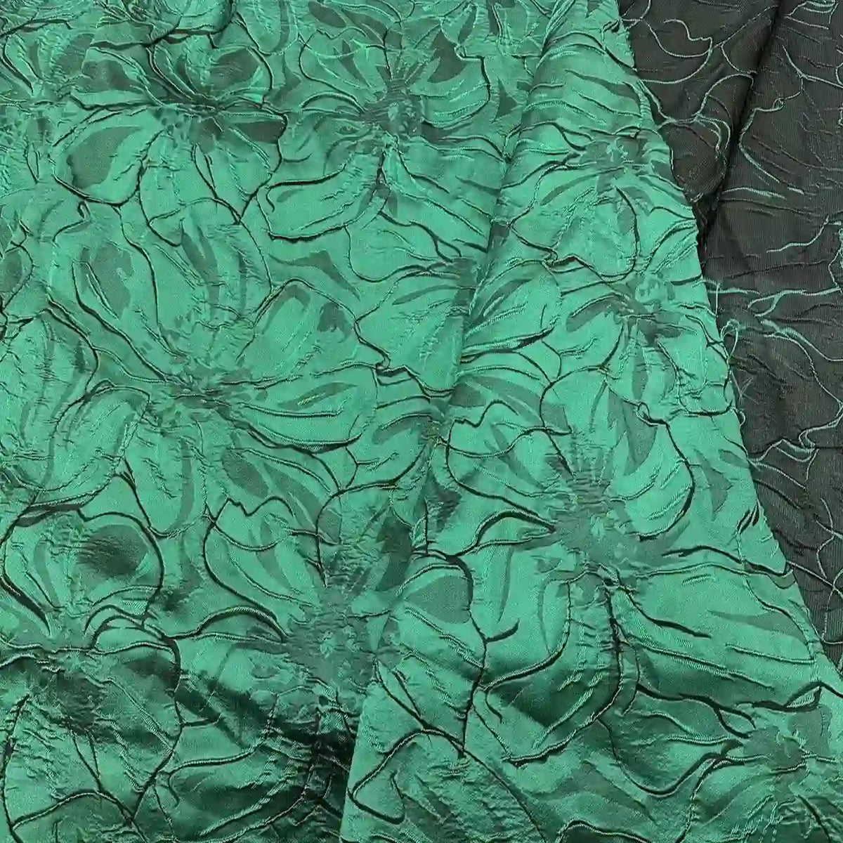 Close-up of Longon Craft’s Floral Embossed Jacquard Brocade Fabric, a shiny green and black polyester with 3D solid flower patterns—ideal for party costumes or tailored suits. Available by the yard.