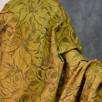 A close-up of Longon Craft's Floral Embossed Jacquard Brocade Fabric By The Yard shows its 3D solid color flower pattern in golden-green polyester, with elegant folds highlighting the intricate, textured design—perfect for party costumes or tailored suits.
