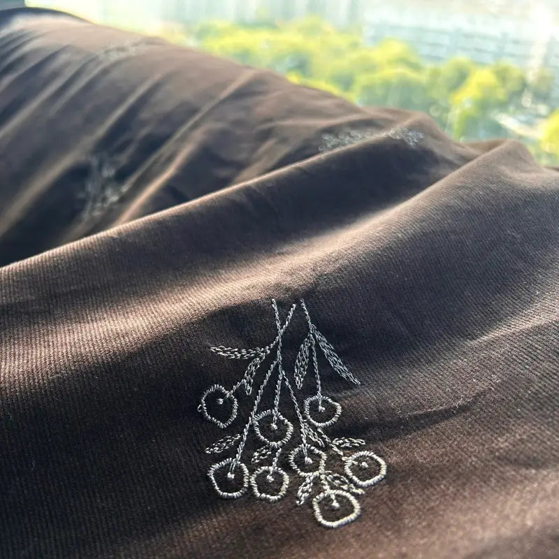 Close-up of Longan Craft's Floral Embroidered Cotton Corduroy Fabric by the yard—Brown Pinwale, featuring a delicate white branch-and-berry pattern and soft autumn texture, shown in sunlight near a window with blurred outdoor scenery.