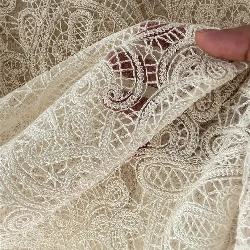 A hand holds Floral Embroidered Lace Fabric By The Yard from Longan craft, a sheer, cream cotton thread material featuring intricate embroidery—perfect for wedding dresses and showcasing timeless elegance.