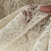 A hand holds Floral Embroidered Lace Fabric By The Yard from Longan craft, a sheer, cream cotton thread material featuring intricate embroidery—perfect for wedding dresses and showcasing timeless elegance.