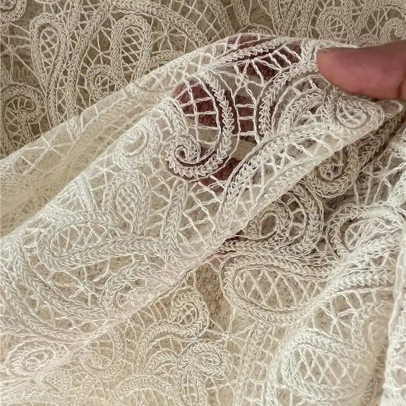 A hand holds Floral Embroidered Lace Fabric By The Yard from Longan craft, a sheer, cream cotton thread material featuring intricate embroidery—perfect for wedding dresses and showcasing timeless elegance.