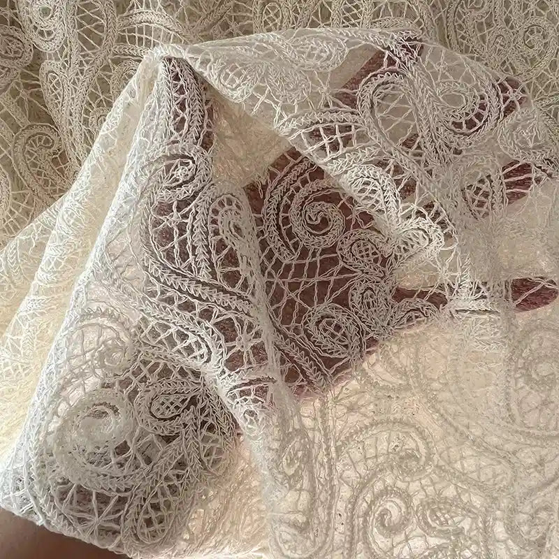 A hand holds Longan craft's Floral Embroidered Lace Fabric By The Yard, showcasing intricate cotton embroidery in ivory—perfect for wedding dresses. The delicate material is semi-sheer, letting the hand partially show through.