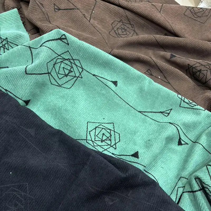 Longan Craft’s Floral Embroidered Polyester Corduroy Fabric features fine wale, black geometric rose patterns on brown, teal, and dark blue. This soft-textured material is ideal for DIY pants and is sold by the yard.