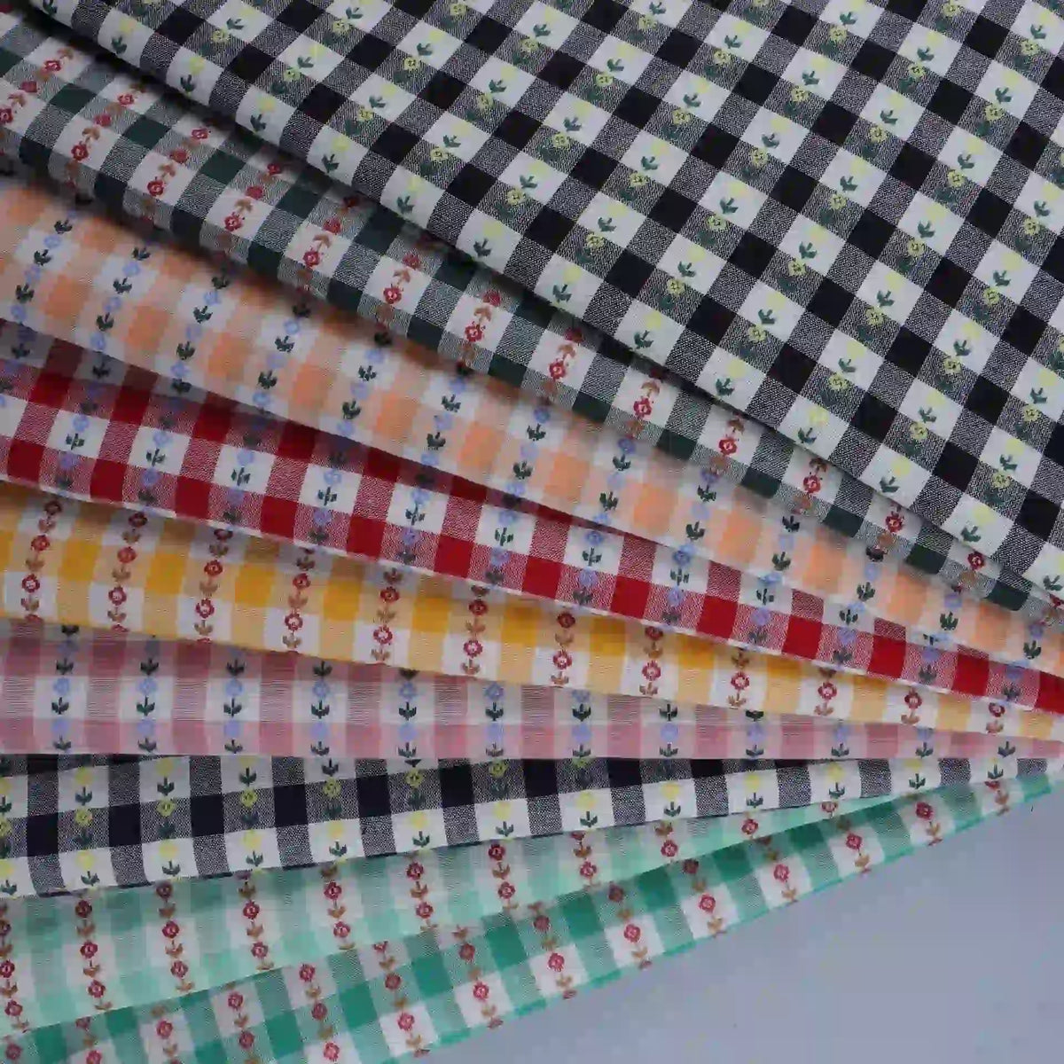 Explore the charming Floral Gingham Poplin Fabric By The Yard from Longan Craft—a collection of colorful cotton checkered jacquard poplin materials featuring gingham plaid patterns in shades of black, orange, yellow, red, and teal. Each piece is beautifully adorned with small floral designs and crafted from soft cotton fabric, making this perfect poplin fabric ideal for a range of creative garment-making and sewing projects.