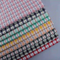 A stack of Floral Gingham Poplin fabrics by Longan Craft, featuring colorful cotton checkered jacquard poplin with charming small floral patterns, is displayed on a light gray surface. These delightful fabrics by the yard are perfect for adding a playful touch to any garment-making or sewing project.