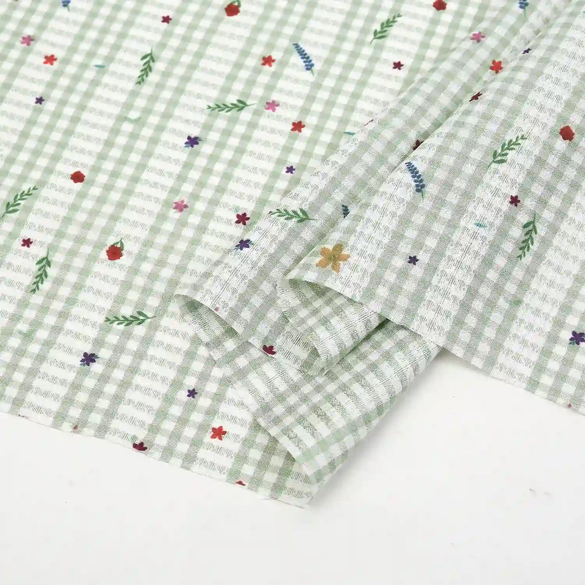 A close-up of Longan Craft's Floral Gingham Quilting Fabric by the yard, a comfy polyester material featuring green-and-white checks with colorful botanical prints, shown with one corner folded over.