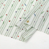 A close-up of Longan Craft's Floral Gingham Quilting Fabric by the yard, a comfy polyester material featuring green-and-white checks with colorful botanical prints, shown with one corner folded over.