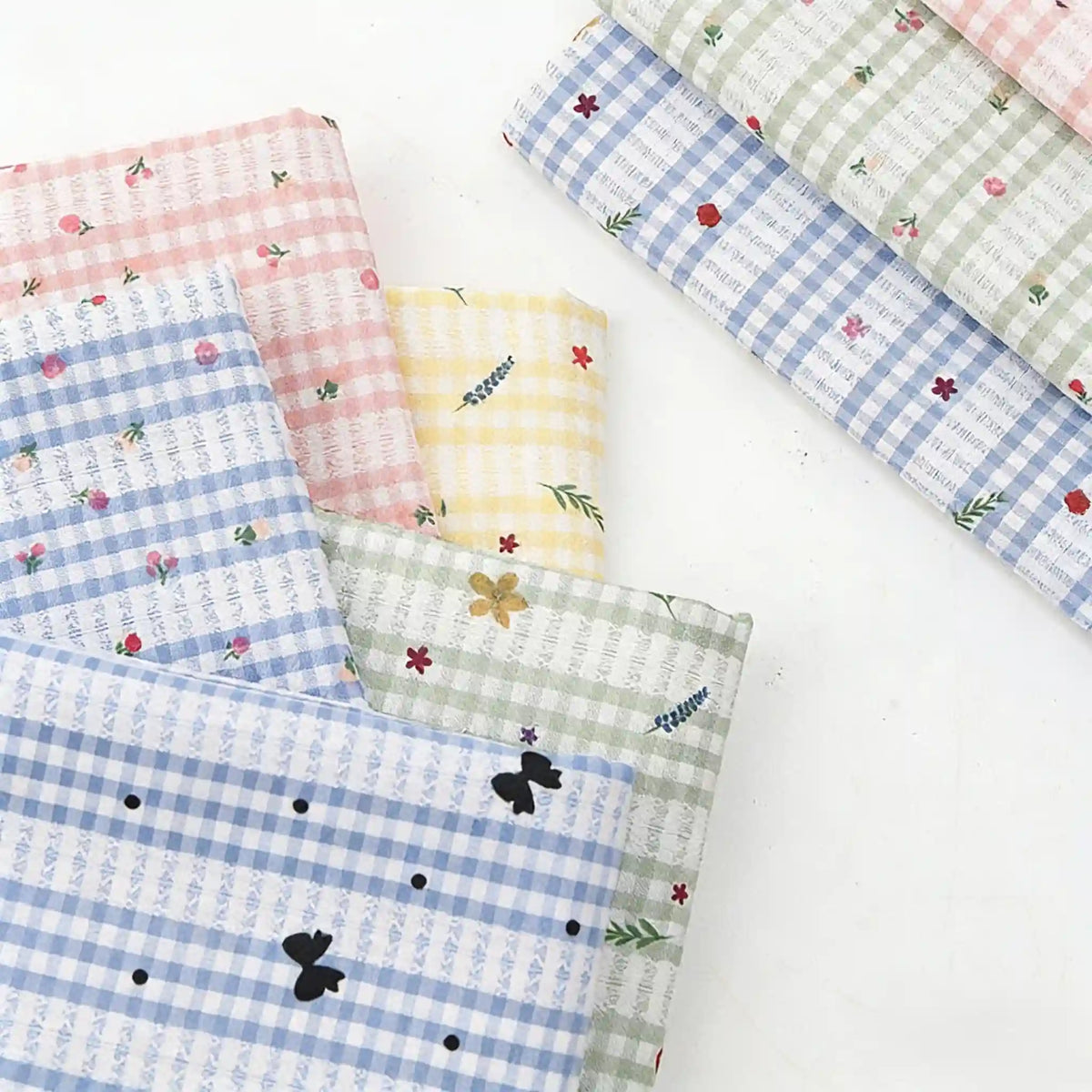 A selection of Longan Craft Floral Gingham Quilting Fabric by the Yard—polyester quilting material with botanical patterns—features overlapping pastel check and floral designs, displayed on a white surface.