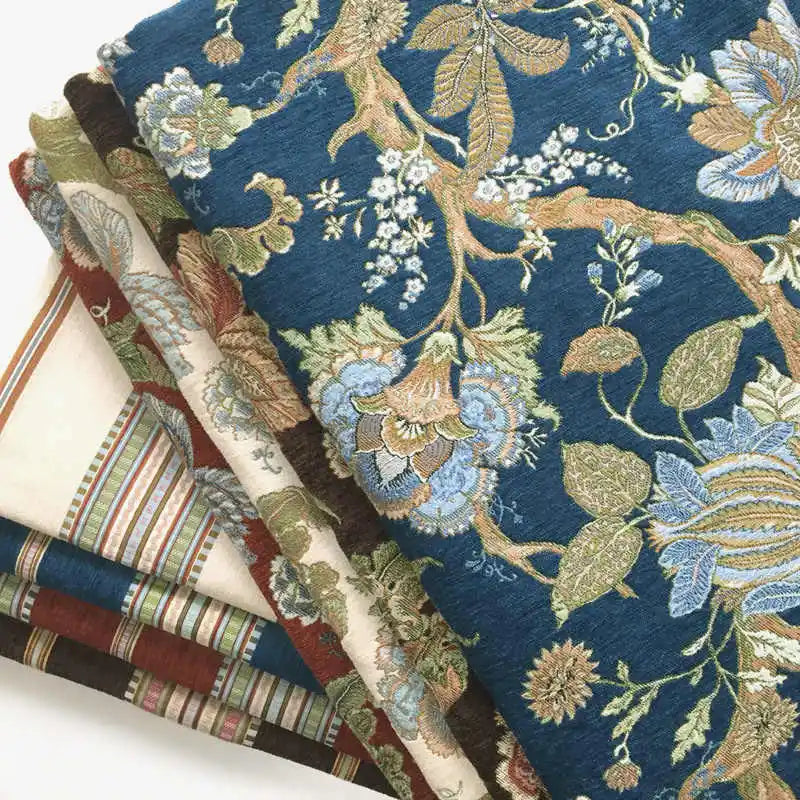 A stack of folded fabrics features Longan Craft’s Floral Jacquard Chenille Fabric by the yard in blue and green on a dark background, alongside striped heavyweight poly chenille upholstery fabric in earthy tones.