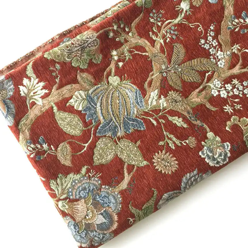 A folded piece of Longan Craft Floral Jacquard Chenille Fabric features a rich red background with intricate blue, green, beige, and brown floral and botanical patterns. Heavyweight poly chenille—perfect for upholstery and home decor.