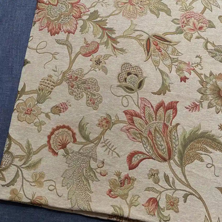 A piece of Longan Craft Floral Jacquard Chenille Fabric By The Yard, a heavyweight poly chenille upholstery fabric with intricate red, green, and beige floral patterns, is displayed on a blue textured surface. Perfect for home decor projects.