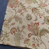 A piece of Longan Craft Floral Jacquard Chenille Fabric By The Yard, a heavyweight poly chenille upholstery fabric with intricate red, green, and beige floral patterns, is displayed on a blue textured surface. Perfect for home decor projects.