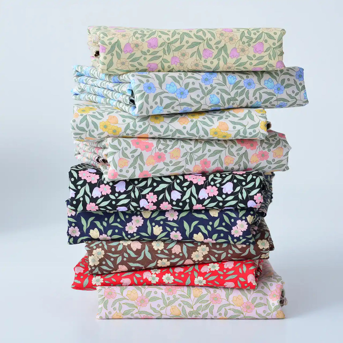 A neatly stacked pile of Longan Craft Floral Lawn Fabric by the yard, in assorted patterns and shades, sits on a light background—lightweight cotton lawn perfect for crafting and lining with breathable style.