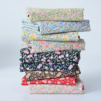 A neatly stacked pile of Longan Craft Floral Lawn Fabric by the yard, in assorted patterns and shades, sits on a light background—lightweight cotton lawn perfect for crafting and lining with breathable style.