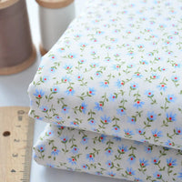 Two folded pieces of Longan Craft Floral Lawn Fabric By The Yard, a lightweight cotton lawn with delicate blue and red floral print, rest beside a ruler and two thread spools—ideal for breathable dresses or linings.