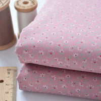 Two folded pieces of pink Floral Lawn Fabric by the yard from Longan Craft, featuring small white and red flowers. Shown with a wooden ruler and brown and white thread spools. Ideal lightweight cotton fabric for lining or sewing projects.