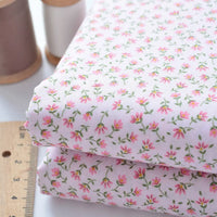 Longan Craft’s Floral Lawn Fabric By The Yard: two folded pieces of lightweight cotton lawn in a delicate pink floral print, with tan and white thread spools and a wooden ruler. Perfect breathable fabric for dresses or linings.