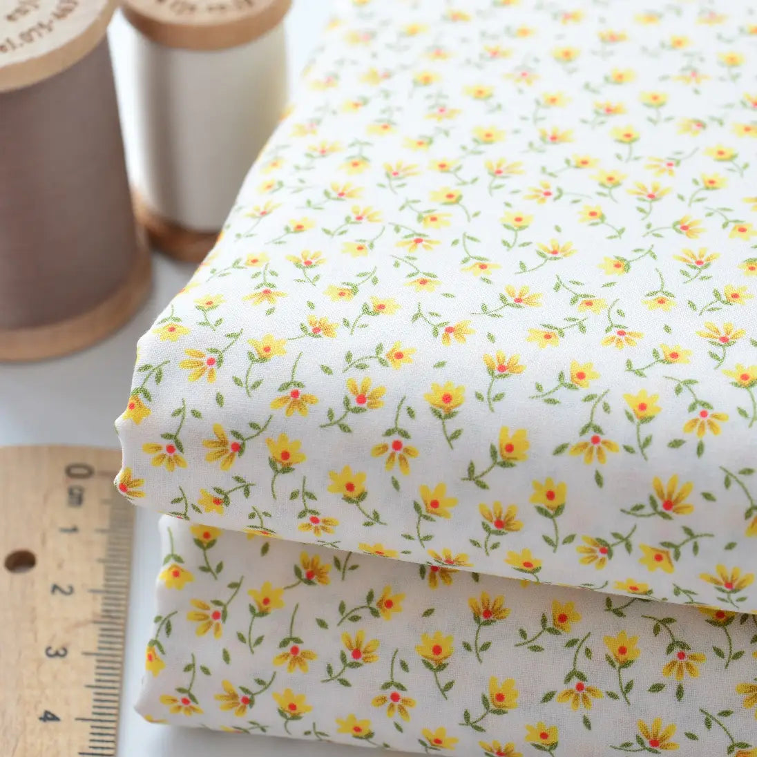 Two folded pieces of Longan Craft Floral Lawn Fabric By The Yard, lightweight cotton with a yellow and green floral print, shown with a ruler and beige/light brown thread—ideal for breathable dresses or cotton lawn projects.