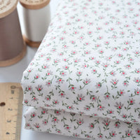 Longan Craft Floral Lawn Fabric by the Yard: lightweight cotton with a small pink and green floral pattern—ideal for breathable dress projects. Shown folded beside wooden thread spools and a ruler. Perfect as lining or dress fabric.