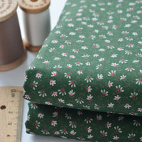 Two folded pieces of Longan Craft Floral Lawn Fabric By The Yard in green with white and pink floral patterns are shown beside a ruler and thread—ideal lightweight cotton for breathable dressmaking or lining projects.