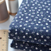 Two folded pieces of Longan Craft Floral Lawn Fabric By The Yard, a lightweight cotton with a small white floral pattern, are stacked on a surface beside a spool of thread and a wooden ruler.