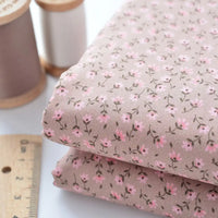 Two folded pieces of Longan Craft Floral Lawn Fabric By The Yard, lightweight cotton with small pink floral patterns, shown beside a ruler and two thread spools. Ideal for breathable dressmaking or as cotton lawn lining fabric.