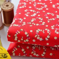 Two stacked pieces of Longan Craft Floral Lawn Fabric—lightweight cotton with a white and pink floral pattern—are shown beside brown thread spools and a yellow measuring tape. Perfect for lining or sewing by the yard.