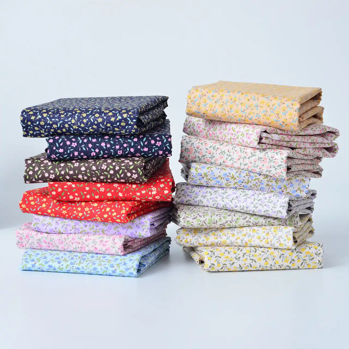 Two stacks of Longan Craft Floral Lawn Fabric By The Yard, featuring lightweight cotton in assorted floral colors and patterns, are arranged on a white surface against a light background. Perfect for lining or sewing projects.