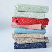 A stack of Longan Craft Floral Lawn Fabric by the Yard—lightweight cotton with small floral patterns—in assorted colors, neatly folded and arranged on a plain background.