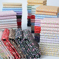 Neatly folded stacks of Longan Craft's Floral Lawn Fabric By The Yard showcase vibrant red, blue, yellow, pink, and green floral prints on lightweight cotton—perfect for breathable projects and organized displays.