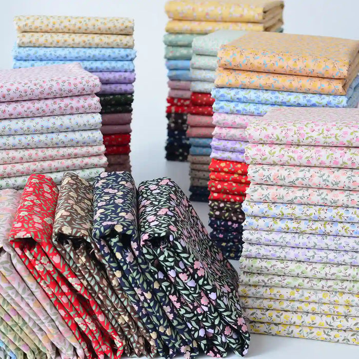 Neatly folded stacks of Longan Craft's Floral Lawn Fabric By The Yard showcase vibrant red, blue, yellow, pink, and green floral prints on lightweight cotton—perfect for breathable projects and organized displays.
