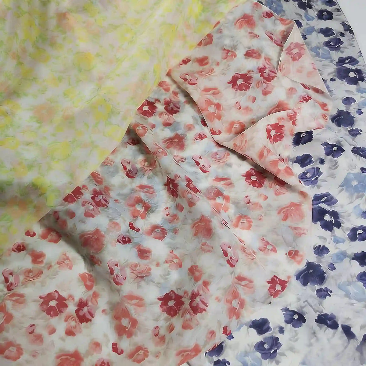 Three sheer fabrics from Longan Craft, including Floral Prin Chiffon Silk Fabric By The Yard, are layered: yellow flowers on top, red and pink blooms in the middle, and blue florals at the bottom—perfect for elegant sheer curtains.