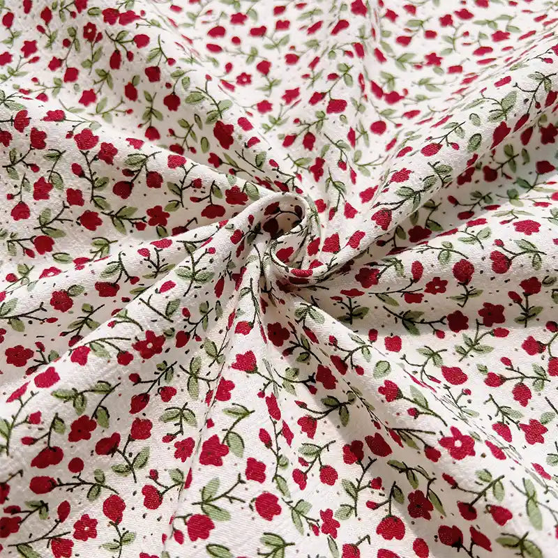 Longan Craft’s Floral Printed Cotton Crepe Fabric By The Yard features a soft washed crepe material adorned with a delicate botanical pattern of small red flowers and green leaves. Gathered in a swirl at the center, the fabric displays gentle folds and texture across its surface, while the evenly distributed floral print adds charm to this comfortable textile—ideal for dresses and creative projects.