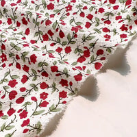 Longan Craft Floral Printed Cotton Crepe Fabric by the yard features a washed crepe material with a botanical pattern of small red flowers and green leaves, showcasing slightly frayed edges and gentle folds for added texture—perfect for comfy dresses.