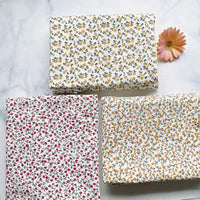 Three pieces of Longan Craft’s Floral Printed Cotton Crepe Fabric By The Yard, featuring botanical patterns in white, yellow, and red, are arranged on a white surface with a pink daisy flower placed nearby.