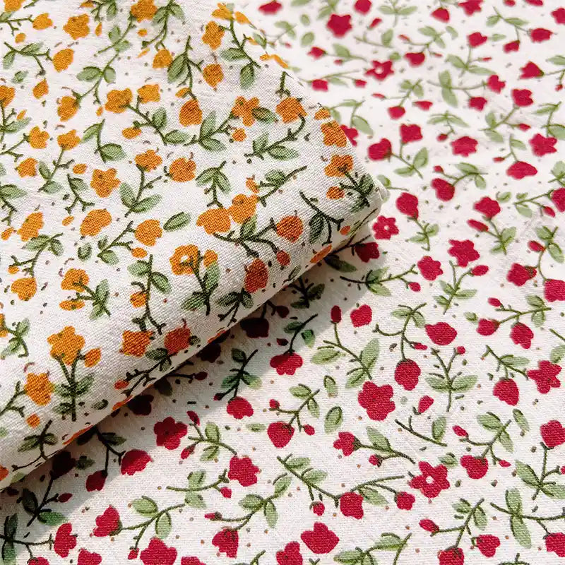 Two pieces of white Floral Printed Cotton Crepe Fabric by Longan Craft, each featuring a small botanical pattern: one with yellow-orange flowers and one with red flowers, both with green stems and leaves. This comfy washed crepe material is ideal for dresses.