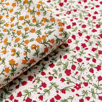 Two pieces of white Floral Printed Cotton Crepe Fabric by Longan Craft, each featuring a small botanical pattern: one with yellow-orange flowers and one with red flowers, both with green stems and leaves. This comfy washed crepe material is ideal for dresses.