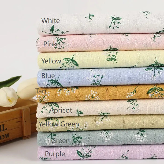 A neatly stacked pile of Longan Craft Floral Printed Dobby Fabric By The Yard, a soft 100% cotton multicolor dobby weave with delicate floral print—perfect for clothing. Tulips and a wooden box sit nearby for added charm.