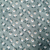 The Longan Craft Floral Printed Peachskin Fabric by the yard features small white flowers with yellow centers and green leaves on a muted green background, printed on soft microfiber polyester peachskin—ideal for comfy apparel projects.