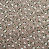 A close-up of Longan Craft’s Floral Printed Peachskin Fabric By The Yard reveals soft microfiber polyester with beige peachskin texture, featuring a repeating print of small white flowers with yellow centers and green leaves.