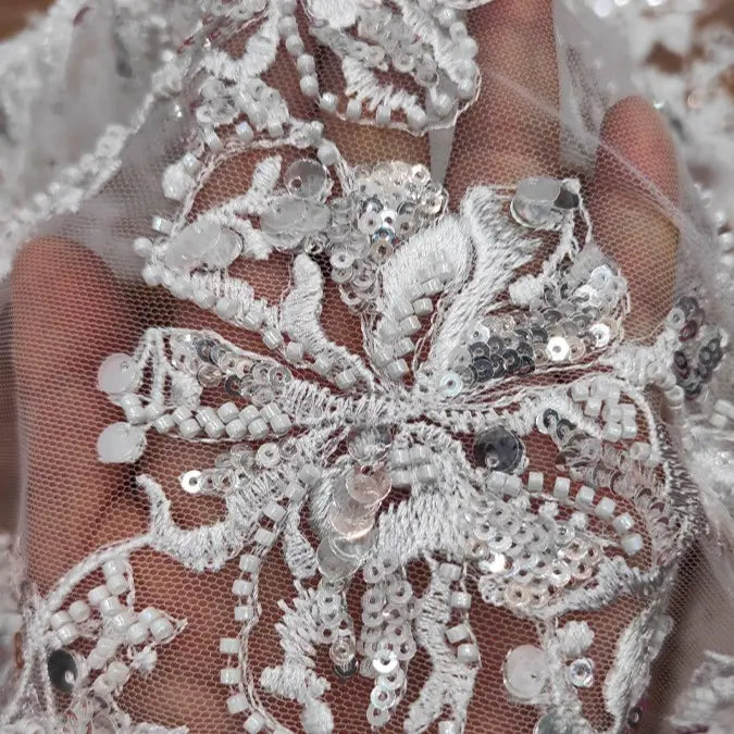 A hand holds Longan Craft’s Floral Sequin Embroidered Tulle Fabric by the yard, a heavyweight material adorned with intricate floral embroidery and sequins—perfect as wedding tulle material.