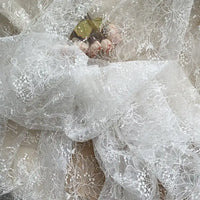 A hand holds Longan Craft's Floral Sequin Lace Fabric By The Yard, a colorful sparkling lace material for dresses, with delicate floral patterns and shimmering sequins partially covering the gold object.