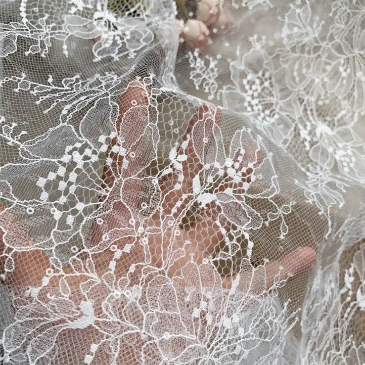 A hand appears behind the Floral Sequin Lace Fabric By The Yard from Longan Craft, emphasizing its colorful sparkling embroidery and sheer texture—perfect lace material for dresses.