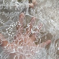 A hand appears behind the Floral Sequin Lace Fabric By The Yard from Longan Craft, emphasizing its colorful sparkling embroidery and sheer texture—perfect lace material for dresses.