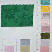 A Longan Craft Floral Polyester Satin Fabric sample card displays a large green floral-patterned swatch left, with twelve smaller luxury satin jacquard samples in assorted colors and patterns arranged right and bottom.