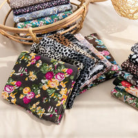 Longan Craft’s Floral and Animal Printed Jersey Fabric by the yard, made from 100% cotton, features vibrant geometric patterns. These fabrics are neatly arranged on a beige surface, with extra breathable material stacked in wicker baskets nearby.