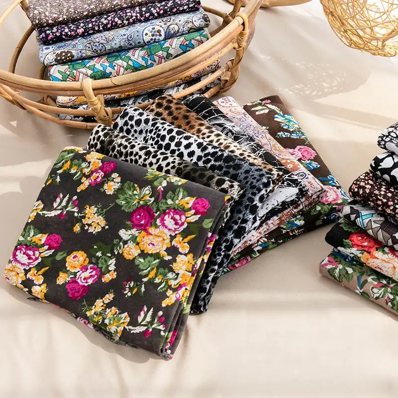 Longan Craft’s Floral and Animal Printed Jersey Fabric by the yard, made from 100% cotton, features vibrant geometric patterns. These fabrics are neatly arranged on a beige surface, with extra breathable material stacked in wicker baskets nearby.